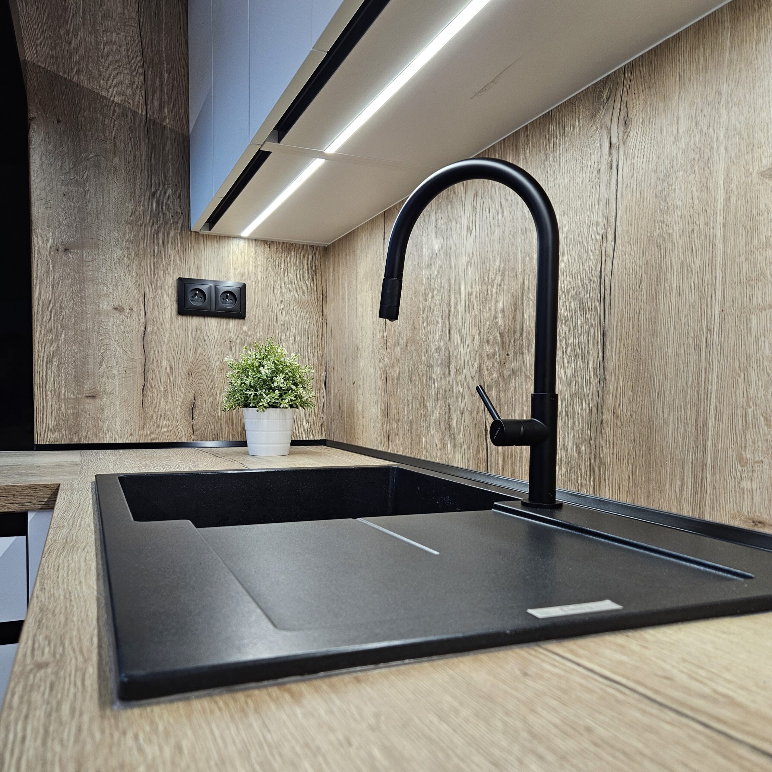 Elegantní kuchyň na míru pro klientku na Smržovce Místo, kde design neustupuje pohodlí. Tato kuchyň spojuje precizní řemeslo s moderními prvky, čímž vzniká harmonický prostor, který je stejně krásný jako funkční. Korpus v odstínu Arktická bílá doplňuje pracovní deska a zadní obklad v dekoru Dub Halifax přírodní, které dodávají interiéru útulnost a přírodní charakter. Spodní skříňky jsou osazeny zápustnými úchytkami Grande v elegantní černé matné, horní části pak využívají subtilní profil S068 v identickém odstínu pro zachování čistých linií. Samozřejmostí je kvalitní kování rakouské firmy Blum, které zajišťuje dlouhou životnost a pohodlné každodenní používání. Kuchyň je dále vybavena luxusními spotřebiči De Dietrich.